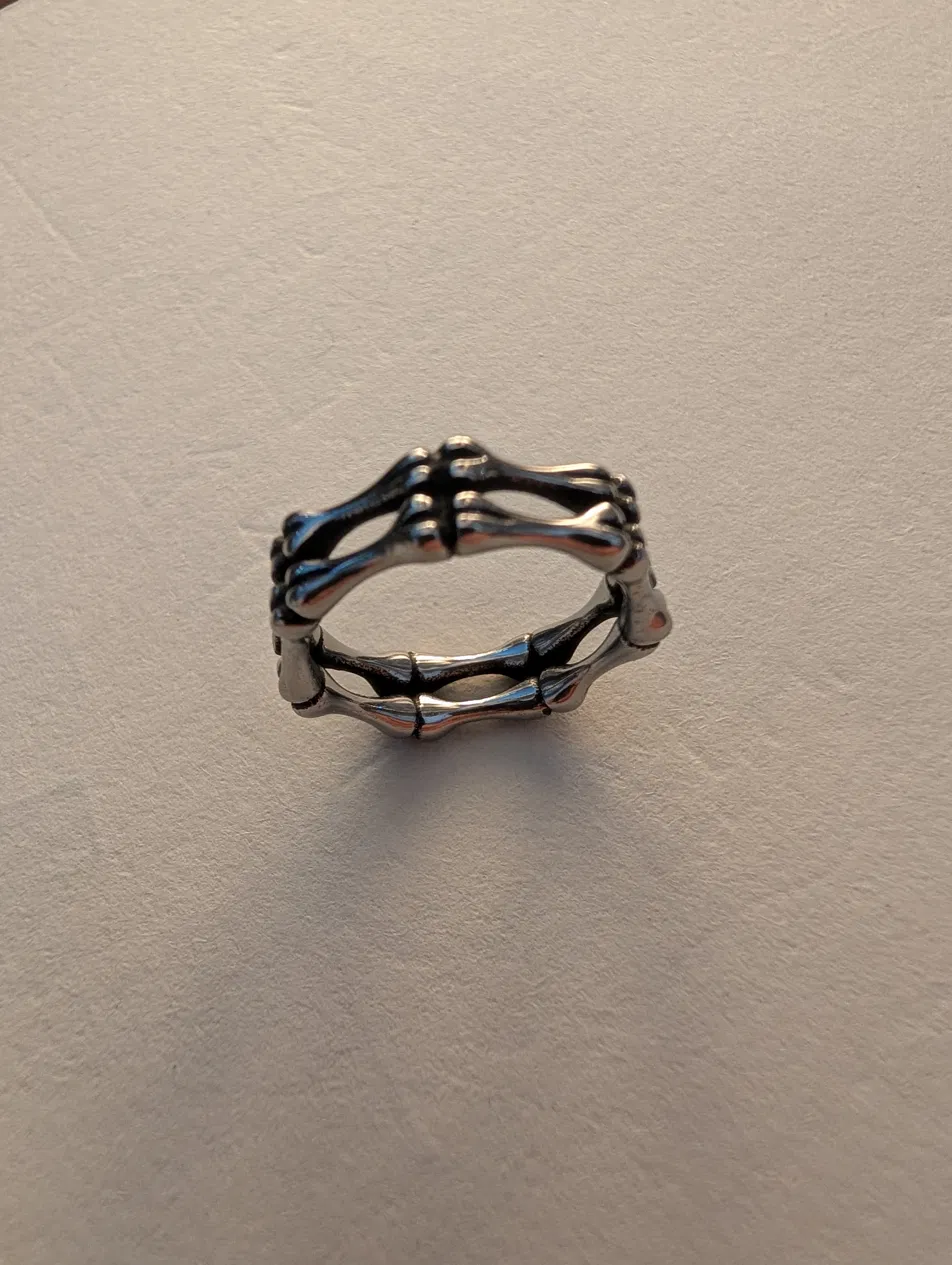 A steel ring cast as two rails of linked finger-bones joined by cross-struts, the oxidised recesses darkened, resting on a pale surface.